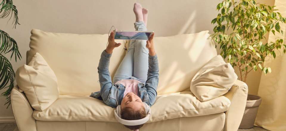 Girl lying on the couch, messing with a tablet and headphones